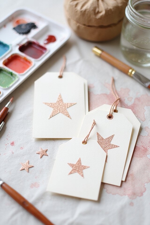 Craft supplies with star tags, watercolor paints, and brushes on a table.