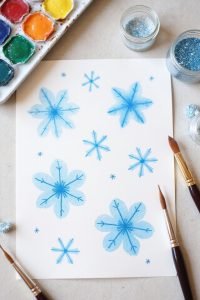 Watercolor snowflakes painting with brushes and colorful palette on a table.
