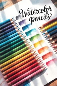 Colorful watercolor pencils with swatches on paper, labeled Watercolor Pencils, lit by sunlight.