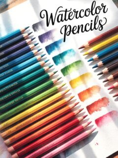 Colorful watercolor pencils with swatches on paper, labeled Watercolor Pencils, lit by sunlight.