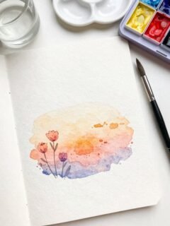 Watercolor painting of flowers on paper with paint palette, brush, and water cup.
