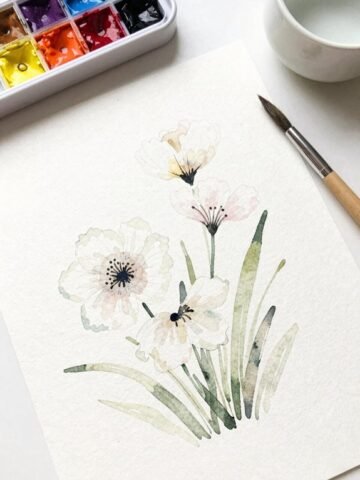Watercolor painting of delicate flowers with a brush and paint palette nearby.